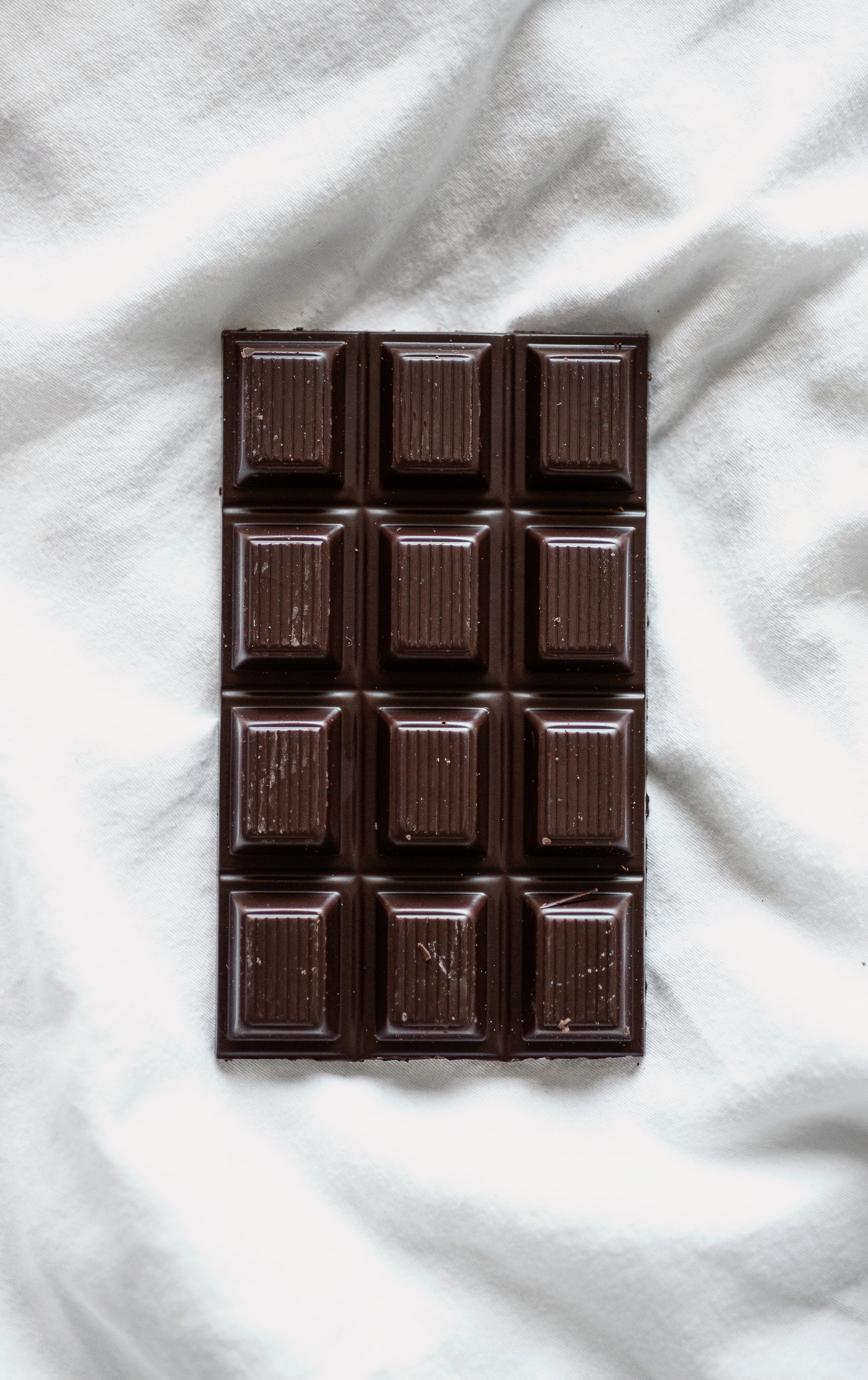 Dark chocolate bar resting on a light fabric surface, shown from above with clean, minimal styling