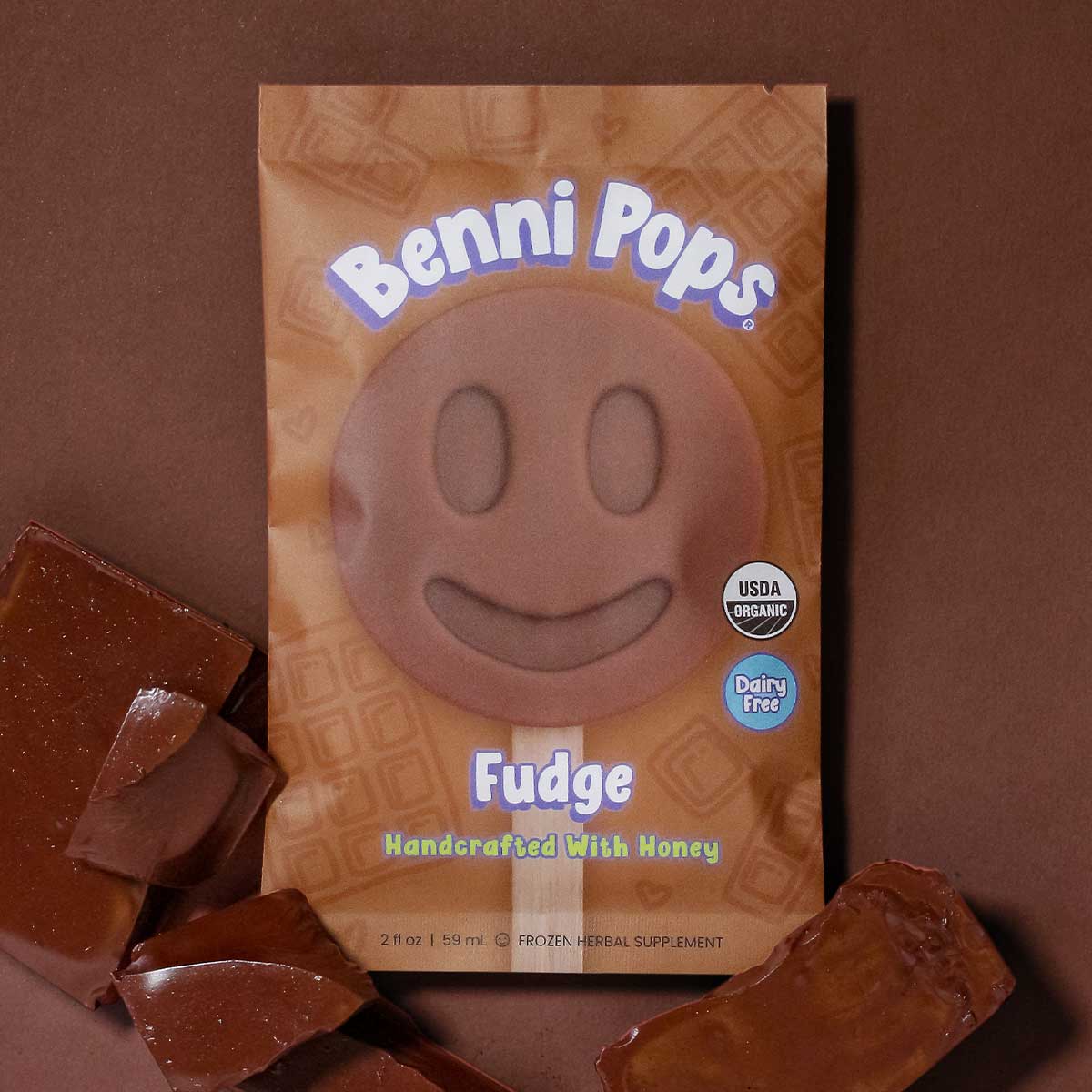Benni Pops Fudge package with smiley face pop and chocolate pieces on a brown background