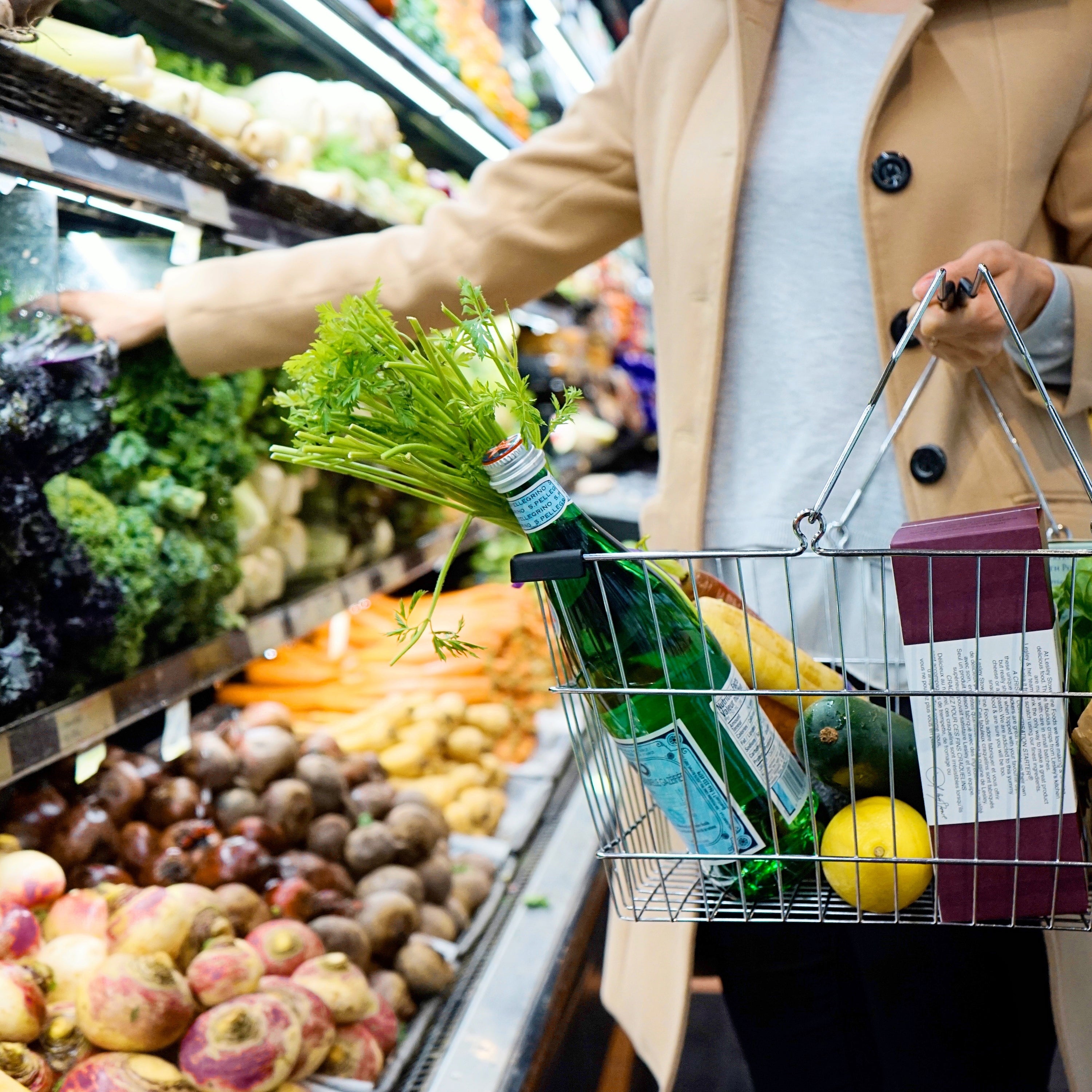 Person shopping for fresh produce in a grocery store, placing vegetables into a wire basket