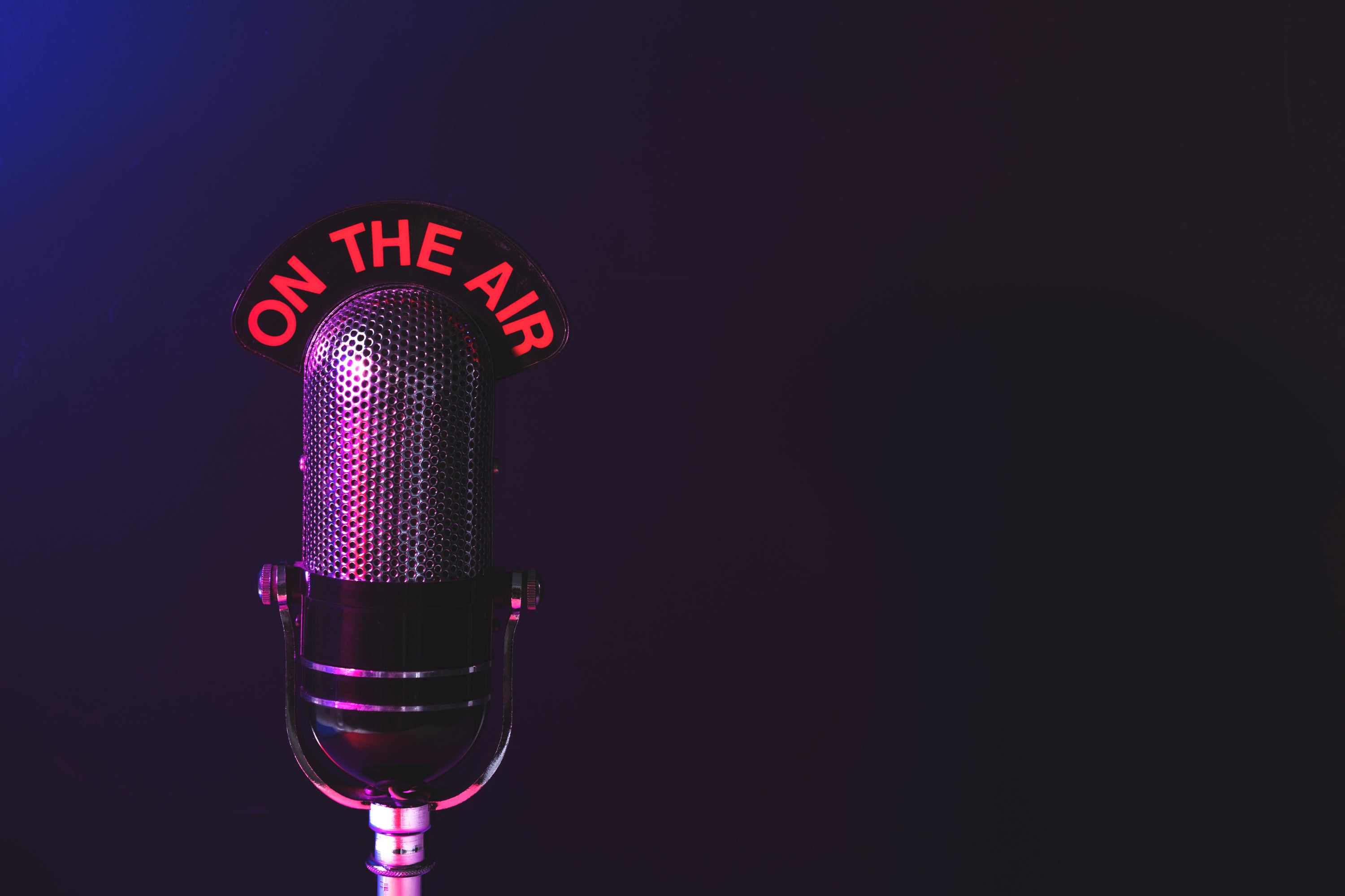 Studio microphone illuminated with an “On the Air” sign, representing interviews, podcasts, or media coverage