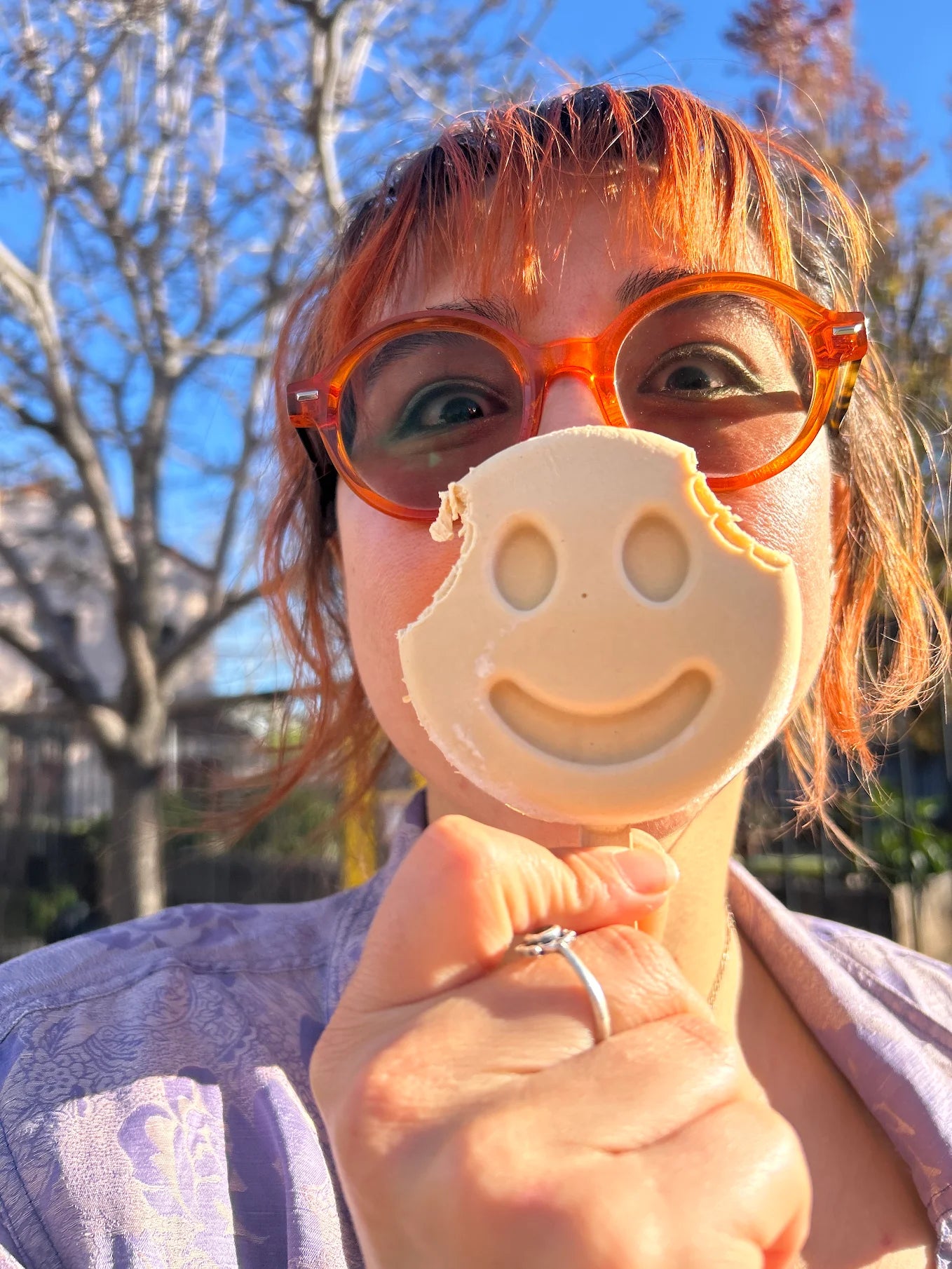 Person wearing glasses holding a light-colored smiley-face frozen dessert