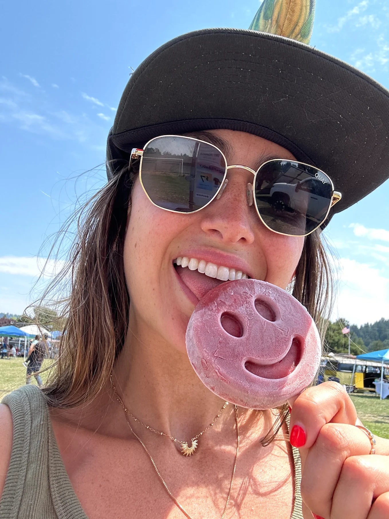 Woman wearing sunglasses holding a smiley-face frozen dessert on a sunny day