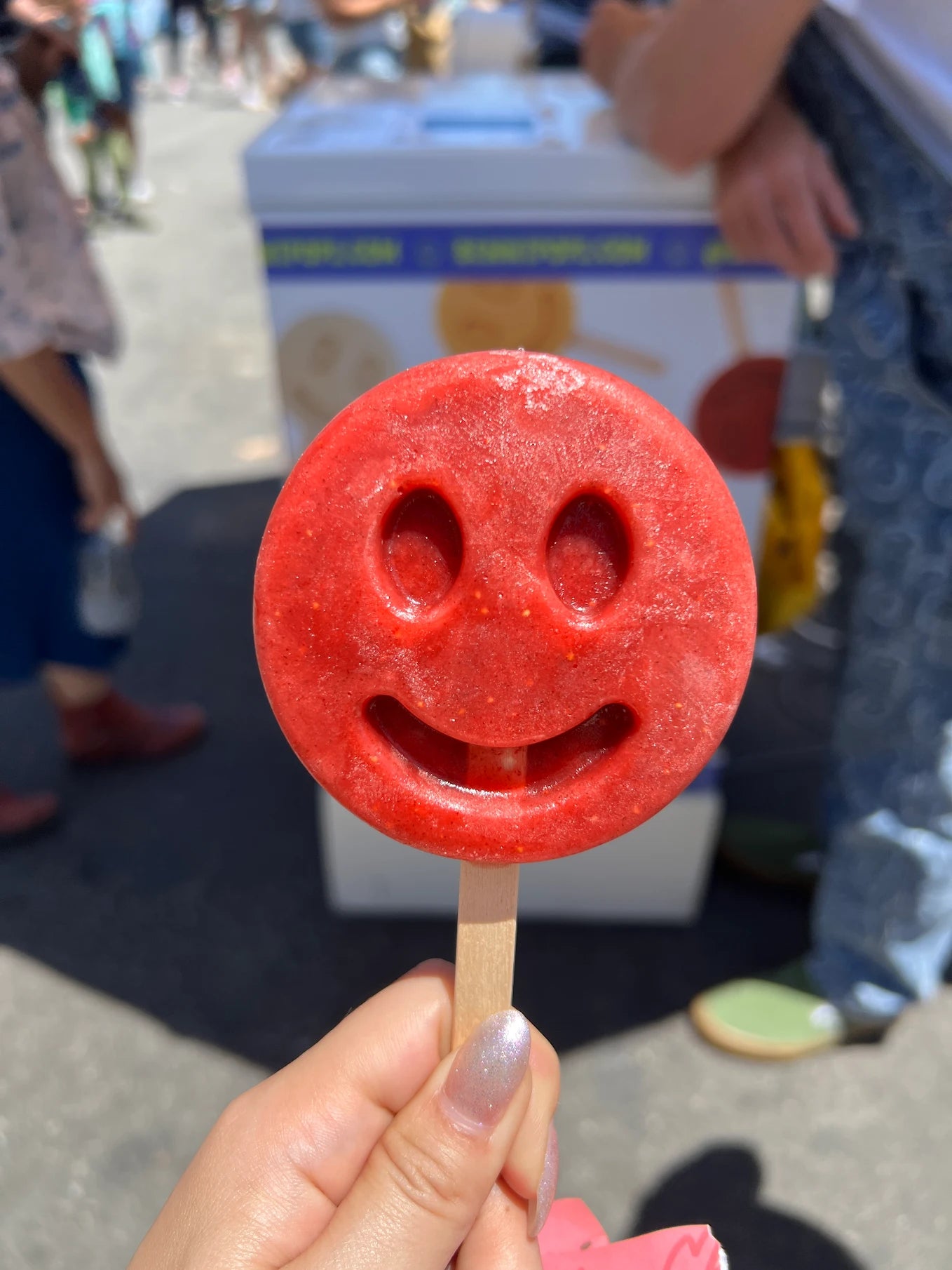 Bright red smiley-face frozen dessert held outdoors in sunlight