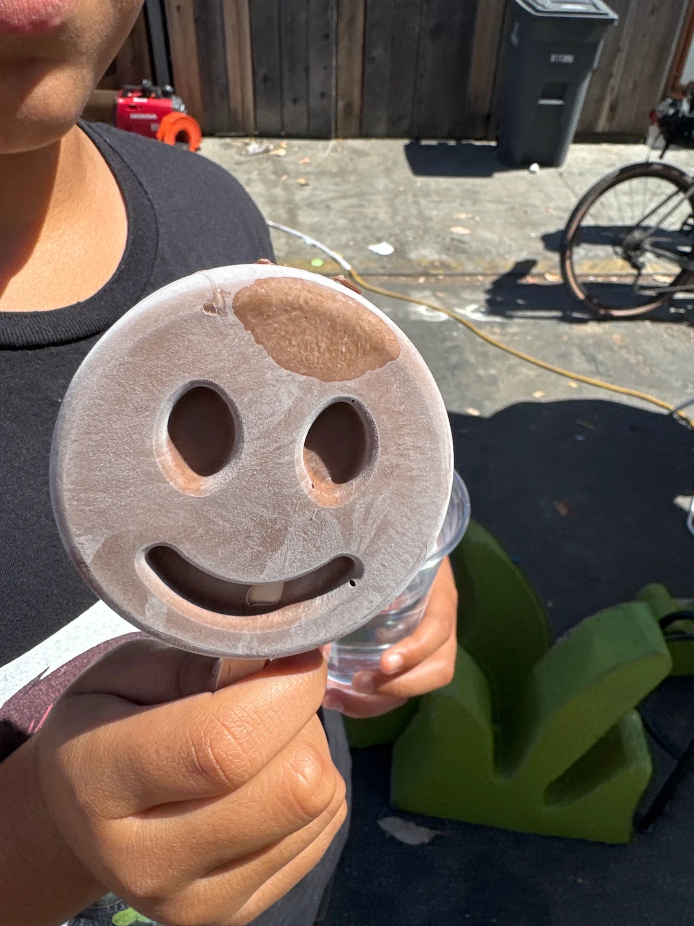 Close-up of a child holding a light-colored smiley-face frozen dessert on a wooden stick