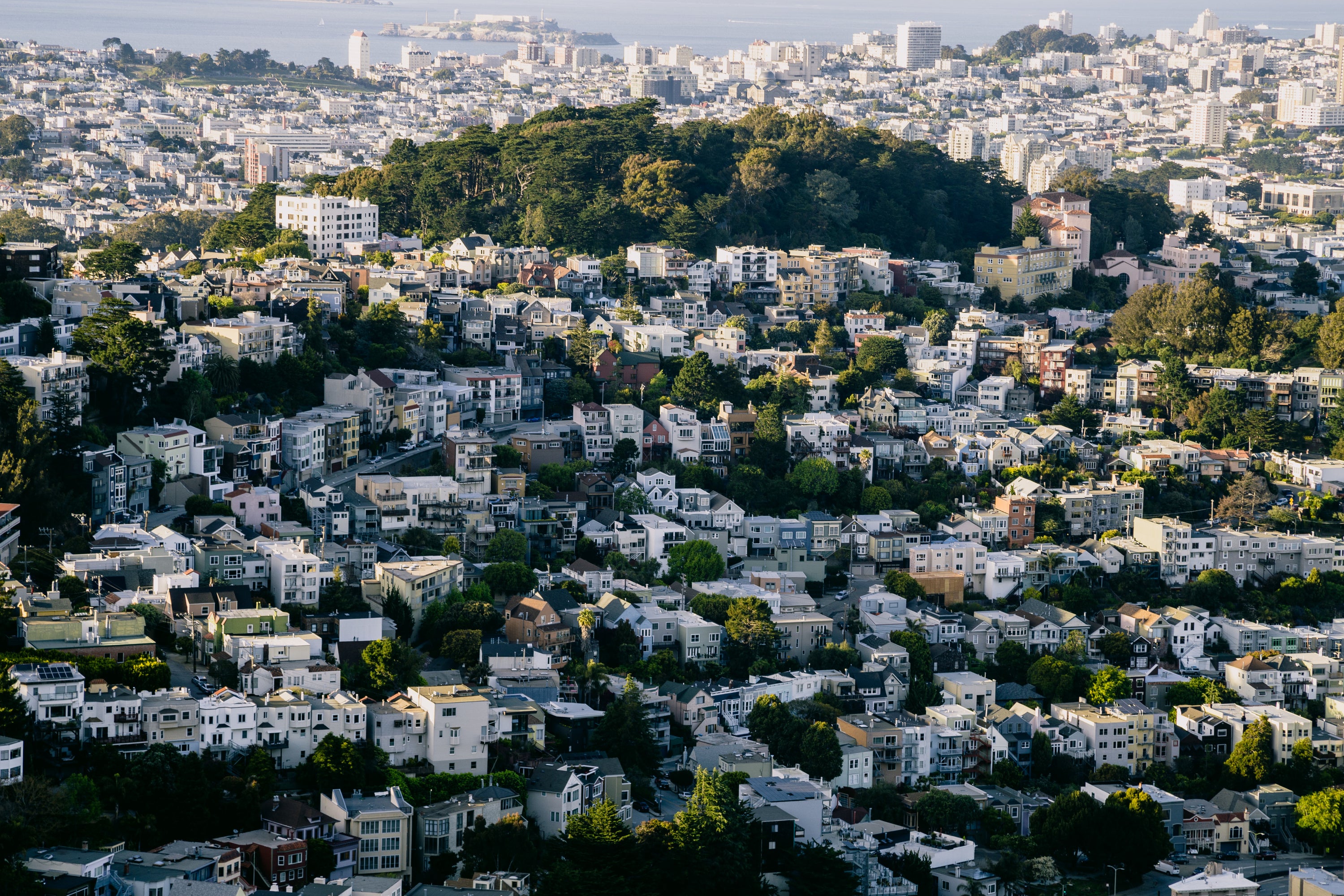 Aerial view of a hillside city neighborhood with dense homes and greenery under clear daylight