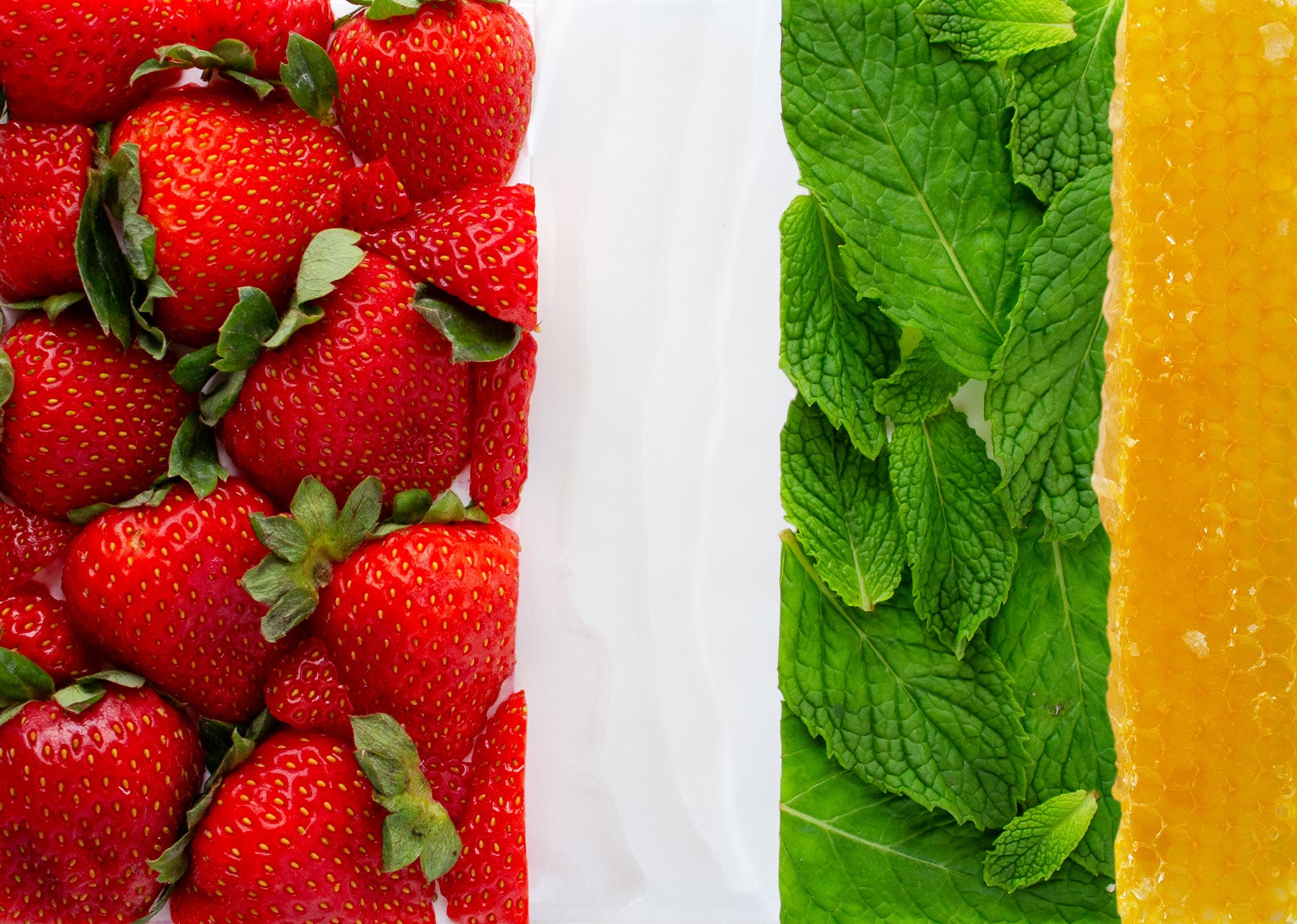 Close-up of strawberries, mint leaves, and orange segments on a white background
