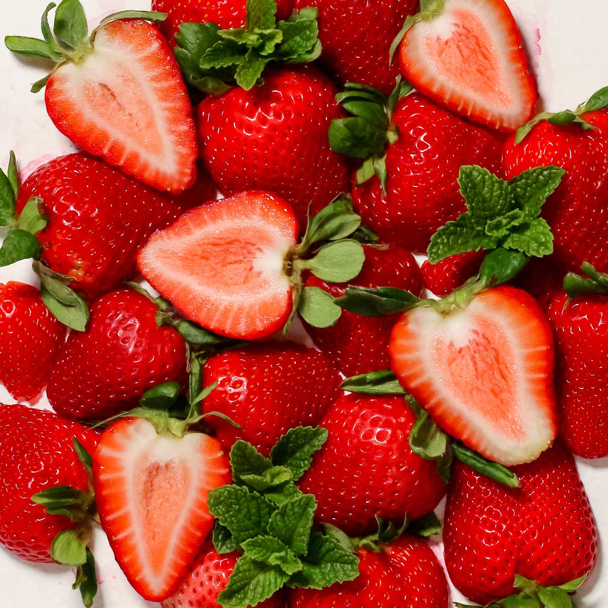 Fresh strawberries with sliced halves and fresh mint leaves arranged closely together