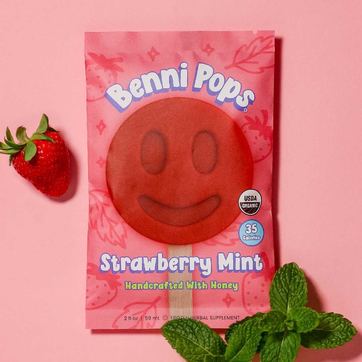 Benni Pops Strawberry Mint frozen dessert in compostable packaging, featuring a red smiley-face treat surrounded by fresh strawberries and mint leaves