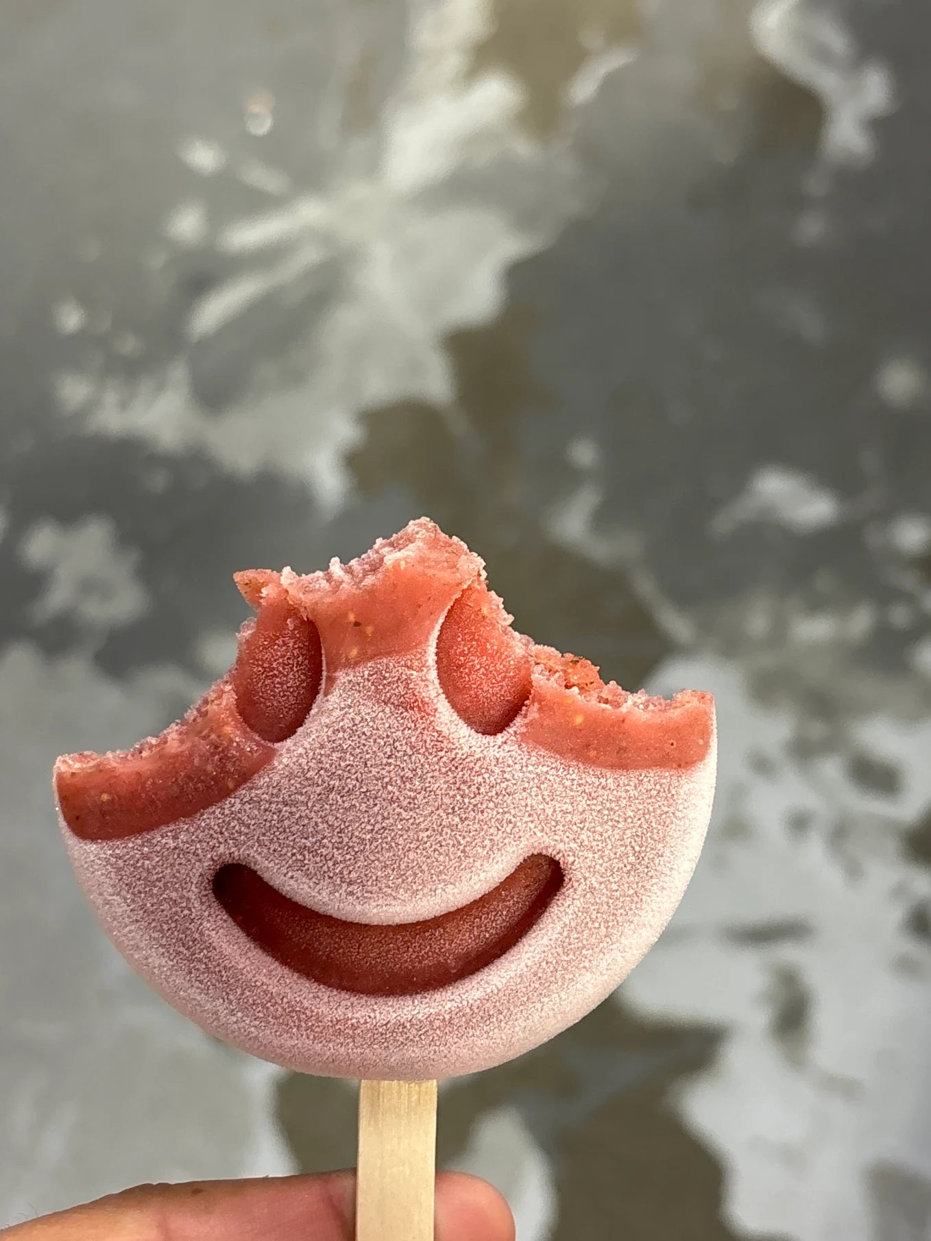 Close-up of a smiley-face frozen dessert held against a neutral background