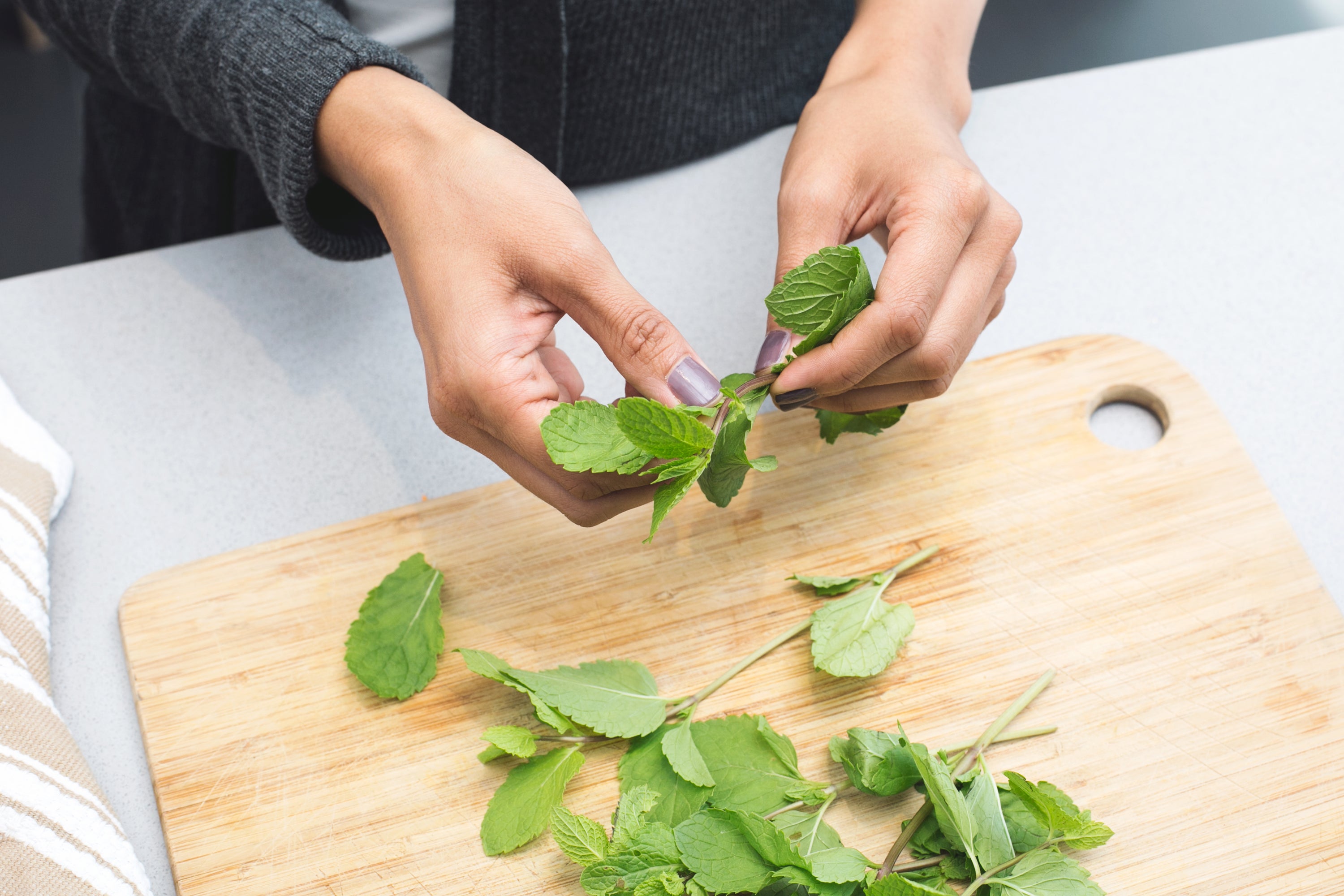 Hands preparing fresh mint leaves on a wooden cutting board, emphasizing freshness and simple ingredients